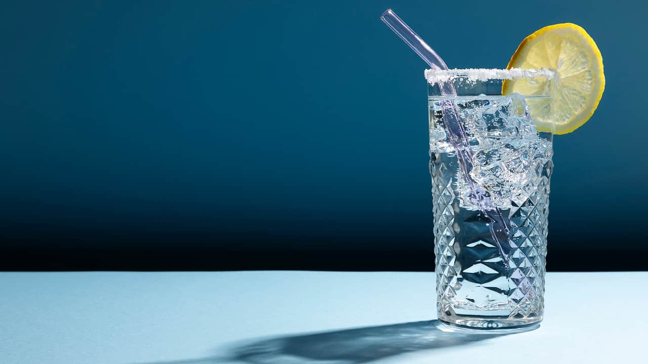 transparent glass filled with sparkling water with a straw and lemon slice